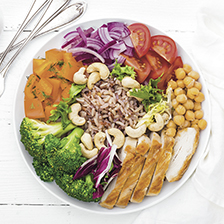 Buddha bowl dish with chicken fillet, brown rice, pepper, tomato, broccoli, onion, chickpea, fresh lettuce salad, cashew and walnuts. Healthy balanced eating.
