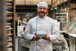 Happy Latin American business owner managing a bakery and using a digital tablet