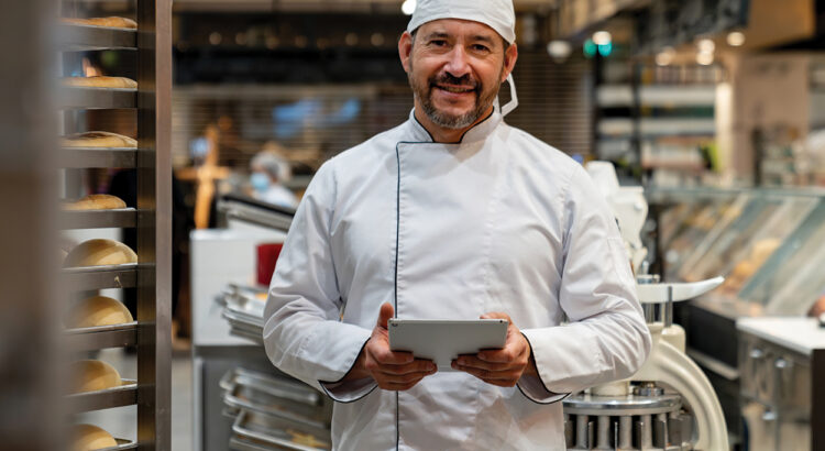 Happy Latin American business owner managing a bakery and using a digital tablet